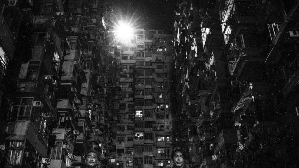 Schwarzweißaufnahme des Filmplakats „Sons of the Neon Night“ vor Hochhäusern.