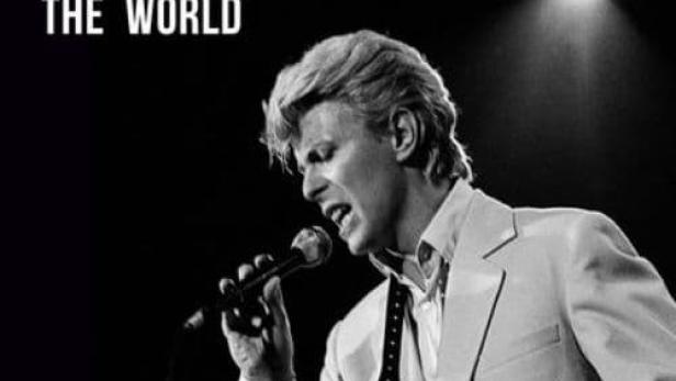 David Bowie singt in einem weißen Anzug auf der Bühne.
