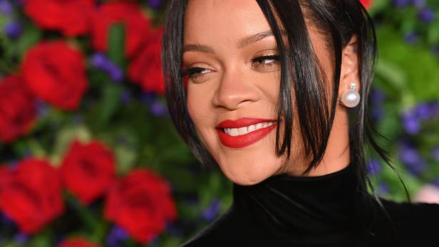 Rihanna lächelt vor einem Hintergrund aus roten und violetten Blumen.