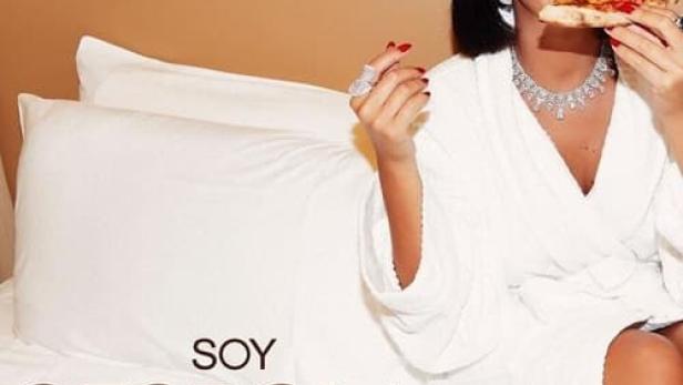 Georgina Rodríguez isst in einem weißen Bademantel Pizza auf einem Bett.