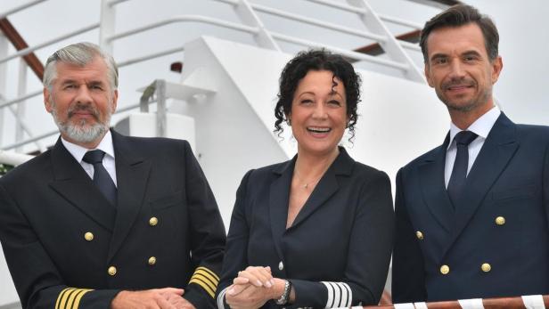 Drei Personen in Marineuniformen stehen auf einem Schiff.