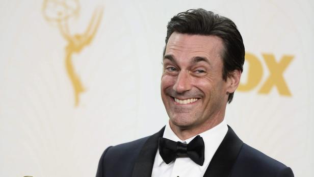Jon Hamm lächelt in einem Smoking vor dem Hintergrund der Emmy Awards.