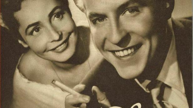 Ein Filmposter für „Kommen Sie am Ersten“ mit einem lächelnden Paar, das Zigaretten hält.