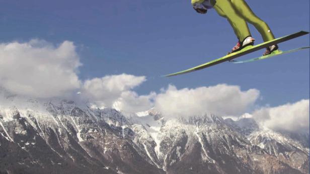 Ein Skispringer in der Luft vor einer Bergkulisse und der Aufschrift „The Big Jump“.