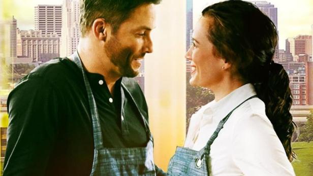 Ein Mann und eine Frau in Kochschürzen stehen vor einer Skyline, Titel: „Farm to Fork to Love“.