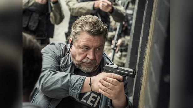 Ein Polizist zielt mit einer Pistole, im Hintergrund weitere Beamte.