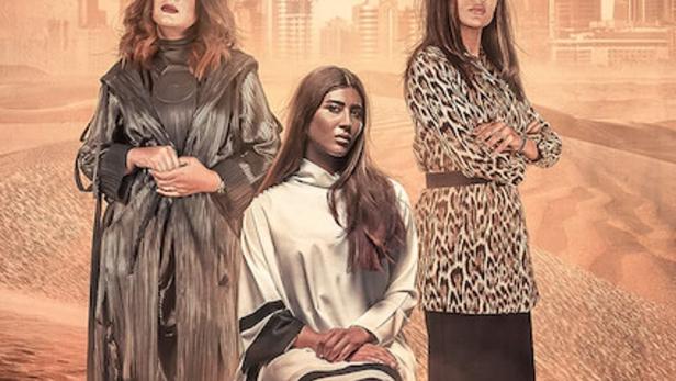 Drei Frauen stehen vor einer Wüstenlandschaft mit einer Stadt im Hintergrund, Titel: „In The Bosom of a Thorn“.