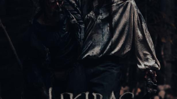 Ein blutverschmierter Mann trägt eine verletzte Person im Horrorfilm „Jikirag: A Pagan Horror“.