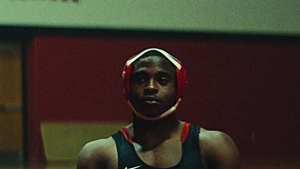 Ein junger Wrestler mit roter Kopfbedeckung und dem Wort „Zion“ im Vordergrund.