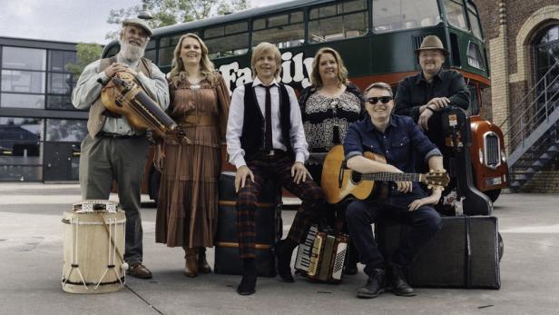Die Kelly Family posiert vor einem Bus mit Musikinstrumenten.