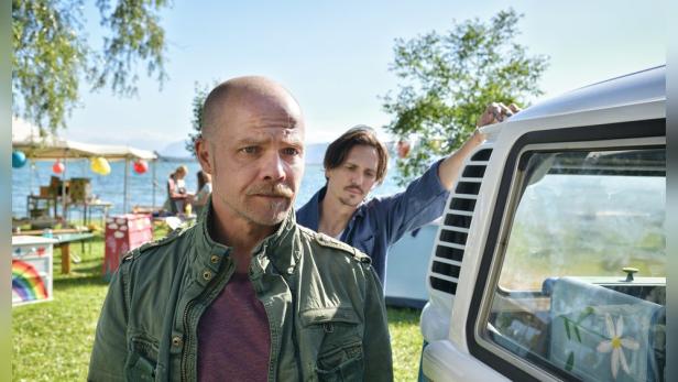 Zwei Männer stehen an einem See neben einem VW-Bus.