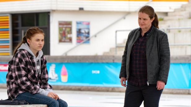 Eine junge Frau sitzt, während eine ältere Frau neben ihr steht.