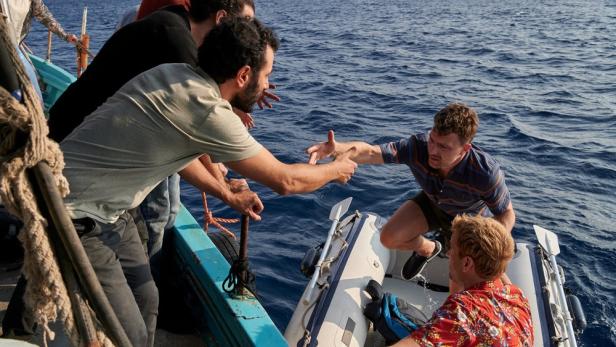 Männer helfen einer Person von einem Boot in ein Schlauchboot auf dem Meer.