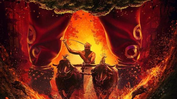 Das Filmplakat für „Kantara“ zeigt einen Mann, der einen von Ochsen gezogenen Wagen durch eine feurige Landschaft lenkt.