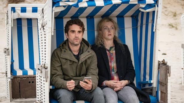 Ein Mann und eine Frau sitzen besorgt in einem blau-weiß gestreiften Strandkorb.