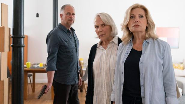 Ein Mann mit einer Pistole steht neben zwei besorgt aussehenden Frauen.