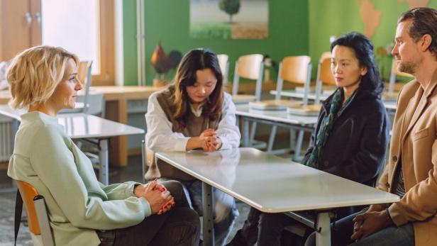 Vier Personen sitzen an einem Tisch in einem Klassenzimmer.