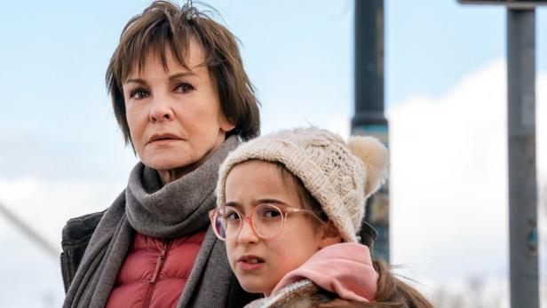 Eine ältere Frau mit einem Schal und ein junges Mädchen mit Brille und Mütze stehen zusammen.