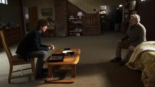 Zwei Männer sitzen sich in einem Wohnzimmer gegenüber und scheinen zu diskutieren.