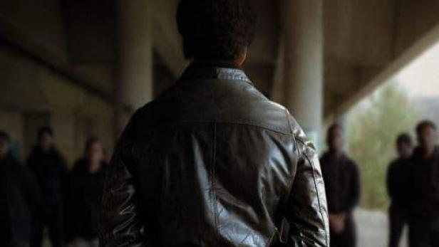 Ein Mann in Lederjacke steht vor einer Gruppe von Menschen, Plakat für den Film „Soldat Noir“.