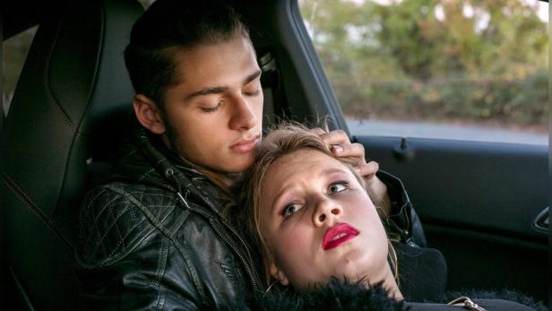 Ein junger Mann schläft, während eine junge Frau mit Make-up neben ihm im Auto liegt.