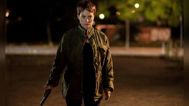 Eine Frau mit einer Schusswaffe in der Hand steht nachts auf einer Straße.