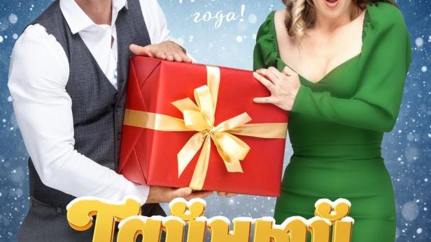 Das Filmplakat für „Tainy Santa“ zeigt Roman Kurtsyn und Zoya Berber mit einem großen, roten Geschenk vor einem Mond mit Weihnachtsmann.