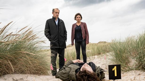 Ein Mann liegt tot am Strand, während zwei Ermittler daneben stehen.