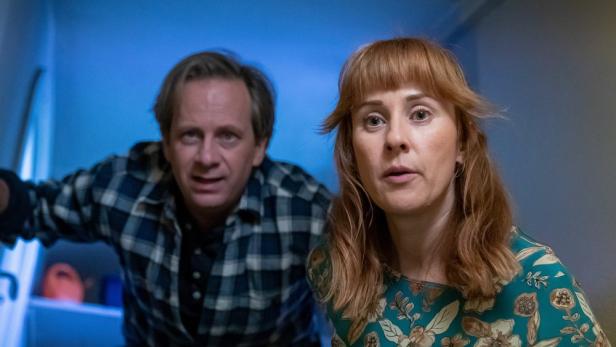 Ein Mann im karierten Hemd und eine Frau mit floralem Oberteil schauen überrascht in die Kamera.