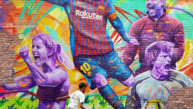 Ein Junge spielt Fußball vor einem Graffiti mit Fußballmotiven, darunter Lionel Messi.