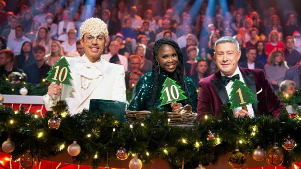 Die Jury der „Let's Dance“-Weihnachtsshow mit Wertungstafeln vor einem festlichen Hintergrund.