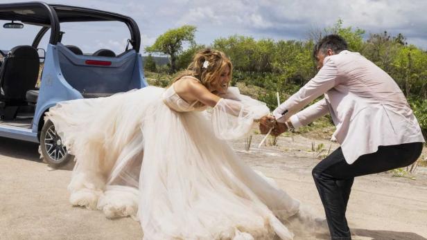 Jennifer Lopez in einem Hochzeitskleid wird von einem Mann weggezogen.