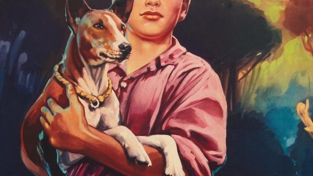Ein Junge hält einen Basenji-Hund mit Halsband vor einem verschwommenen Hintergrund.
