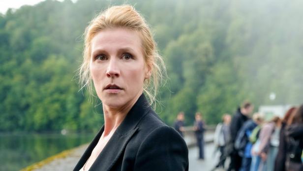 Eine Frau mit blonden Haaren und schwarzem Blazer blickt aufmerksam in die Ferne.