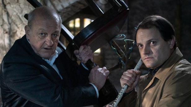 Zwei Männer halten einen Stuhl und eine Stange in einem angespannten Moment aus „Wilsberg – Ungebetene Gäste“.