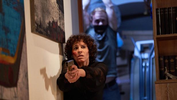 Eine Frau mit Blut im Gesicht zielt mit einer Pistole, während ein Mann im Hintergrund steht.