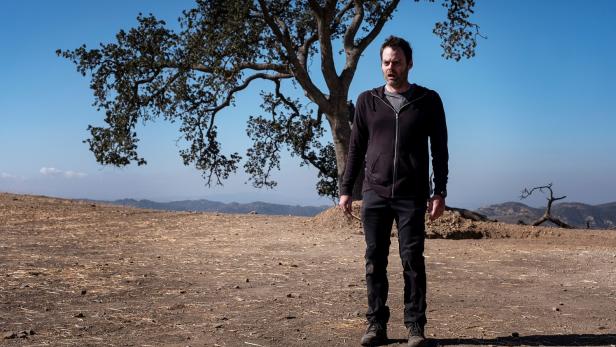 Bill Hader steht vor einem Baum in einer trockenen Landschaft.