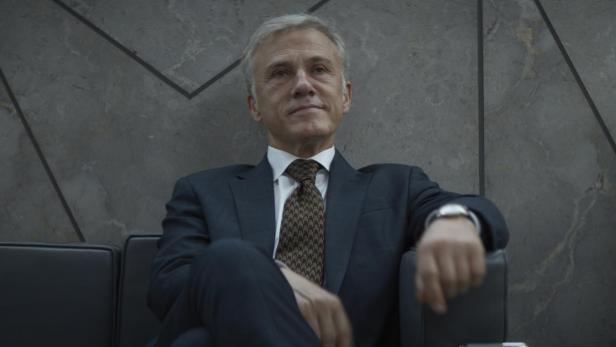 Christoph Waltz in der Serie The Consultant; er sitzt in einem Sessel und lächelt überlegen