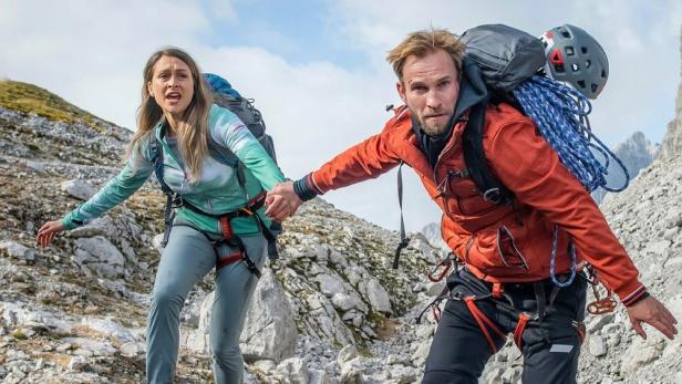 Ein Mann und eine Frau klettern in den Alpen und halten sich an den Händen.
