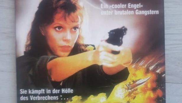 Das Cover des Films „Angel of Hell“ zeigt eine Frau mit einer Waffe vor einer explosiven Szene.