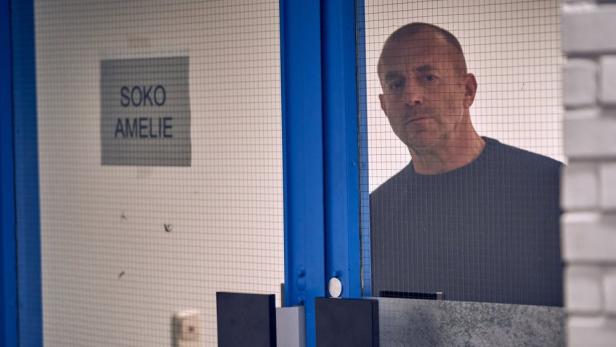 Ein Mann steht hinter einer Tür mit der Aufschrift „SOKO Amelie“.