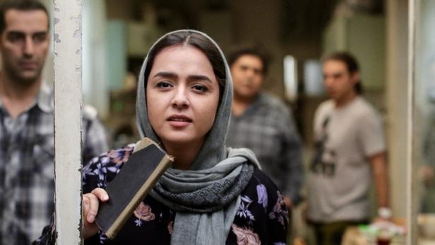 Eine Frau mit Kopftuch hält ein Buch in der Hand, im Hintergrund Männer, möglicherweise eine Szene aus „Leila's Brothers“.