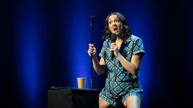 Eine Frau steht auf einer Bühne und spricht in ein Mikrofon.