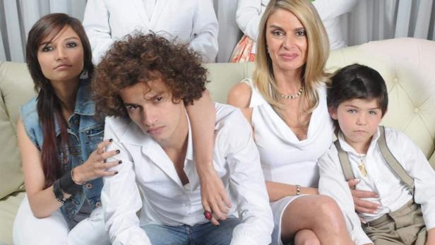 Eine formelle Aufnahme einer Familie, die auf einem Sofa vor einem weißen Vorhang sitzt.