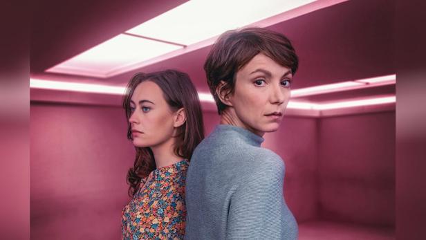 Zwei Frauen stehen vor einem rosafarbenen Hintergrund, möglicherweise ein Filmposter für „Schatten der Angst“.