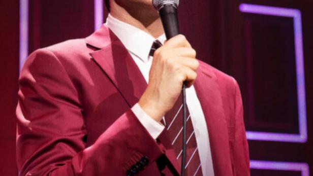 John Mulaney steht mit einem Mikrofon auf der Bühne für „Baby J“.