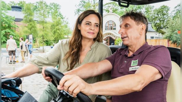 Tierärztin Mertens und ein Mann fahren in einem Golfwagen durch den Zoo.