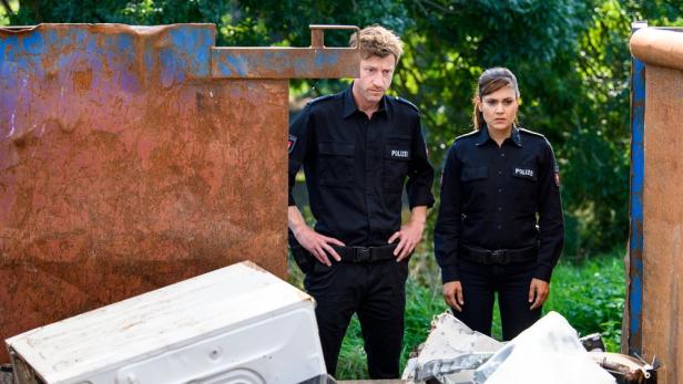 Zwei Polizisten stehen vor einem Container mit Elektroschrott.