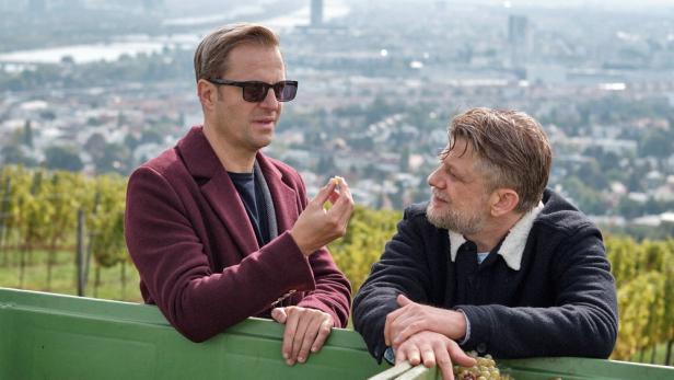 Zwei Männer unterhalten sich in einem Weinberg mit Blick auf die Stadt.