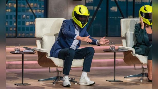 Ein Mann mit gelbem Motorradhelm sitzt in der „Höhle der Löwen“.